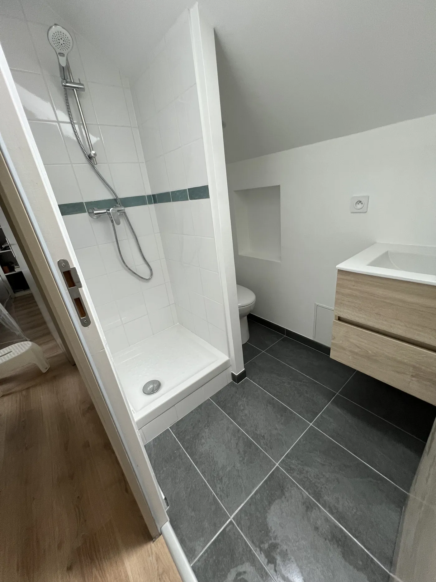 Salle de bain créée à Nantes : douche à receveur, cloison séparant le coin WC, niche de rangement, meuble suspendu bois clair et sol grand format effet ardoise