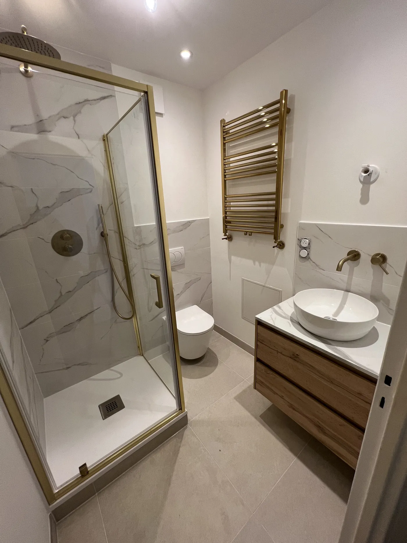 Salle de bain rénovée à Nantes : douche avec paroi et robinetterie laiton brossé, WC suspendu, meuble chêne et vasque à poser, faïence effet marbre