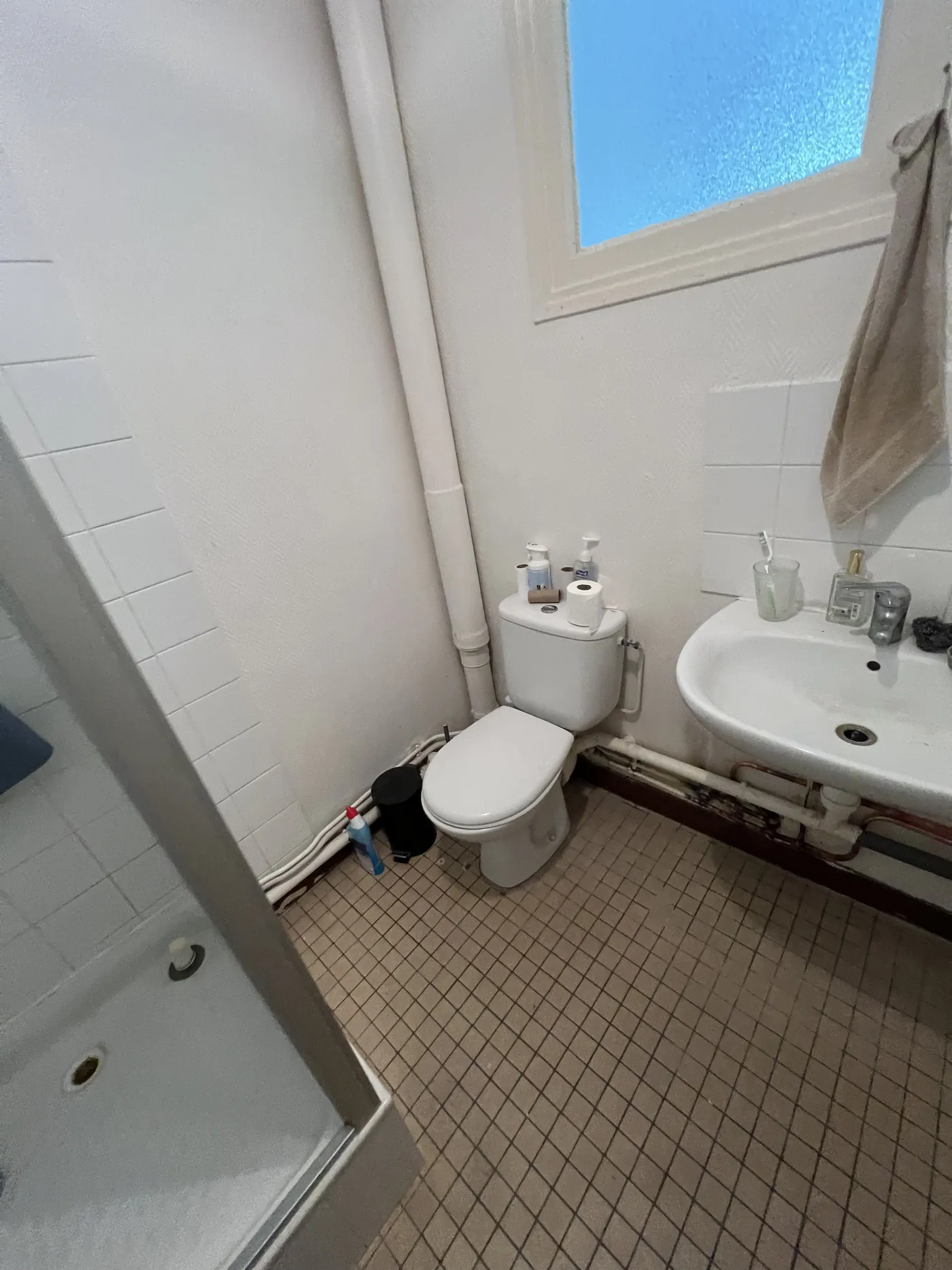 Salle de bain avant rénovation à Nantes : baignoire-douche, WC à poser, lavabo sur colonne, canalisations en applique et carrelage mosaïque beige