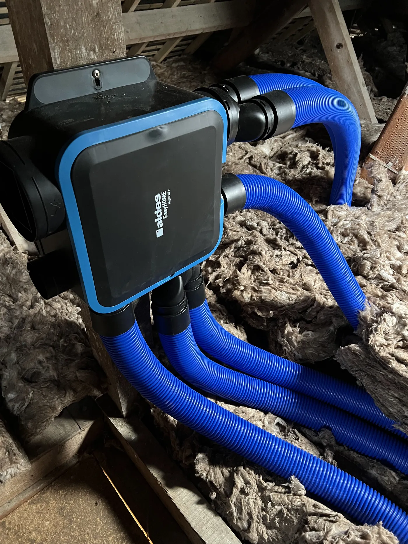 Groupe VMC Aldes EasyHOME Hygro HP+ installé dans les combles d'une maison à Lusanger, cinq piquages raccordés en gaines souples, photographié en cours de pose